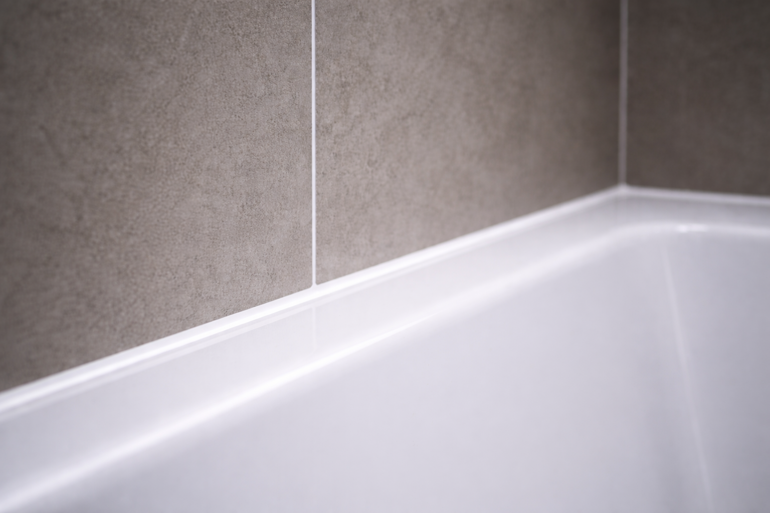 Professionell erneuerte Silikonfuge zwischen grauen Badezimmerfliesen und weißer Badewanne